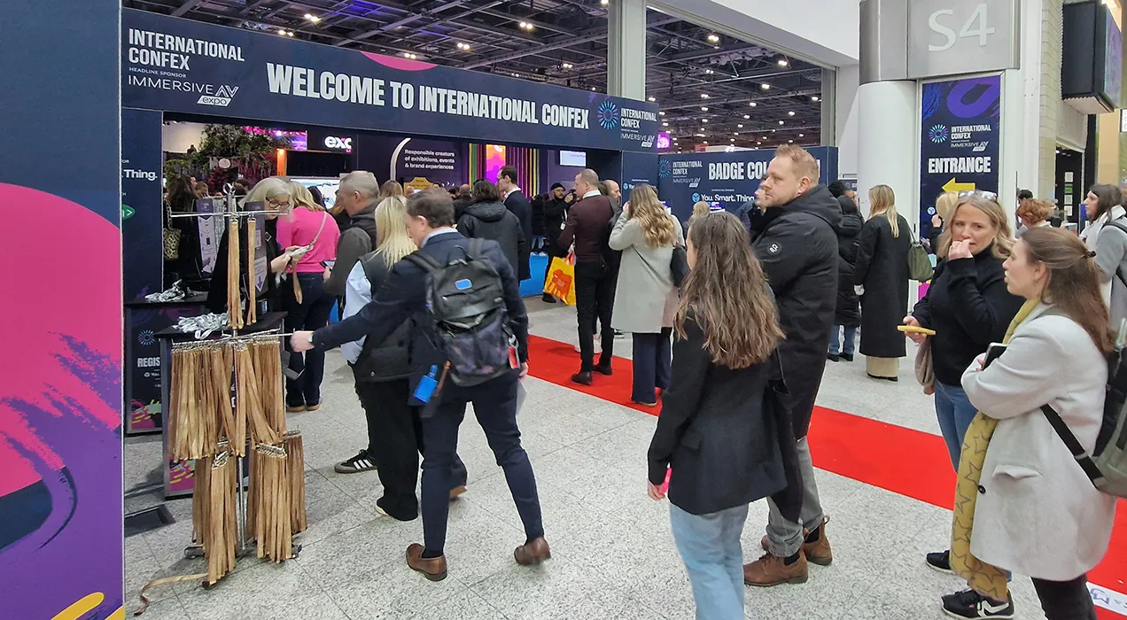 People entering an exhibition, some are collecting their badges from PrintPods