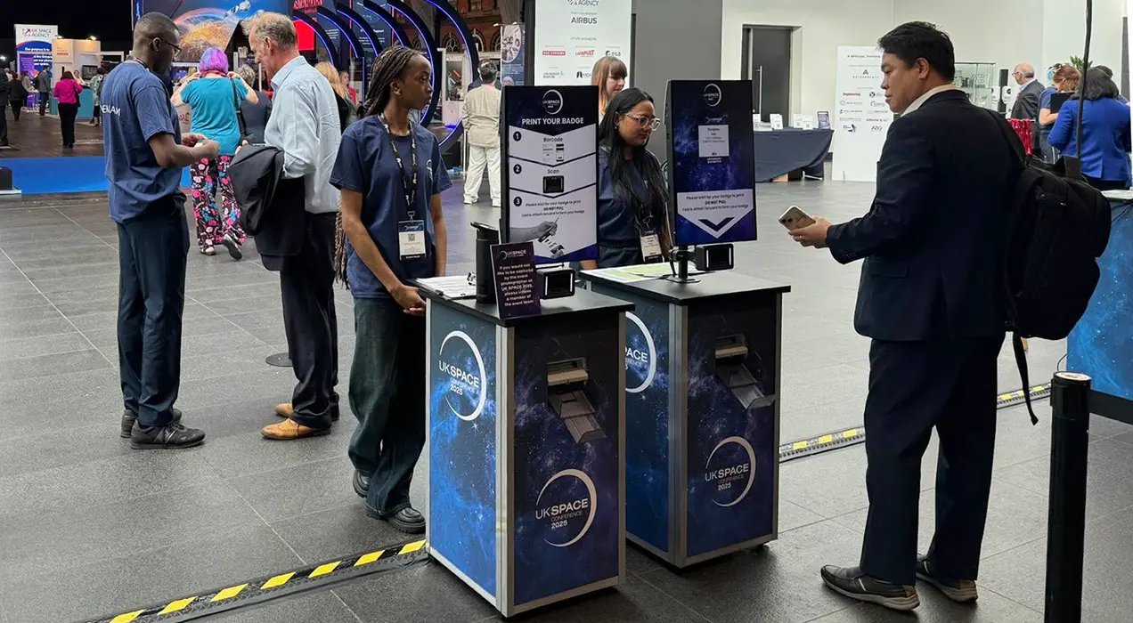 Person scanning the e-badge on their smartphone and collecting their badge from a PrintPod at the entrance to an exhibition
