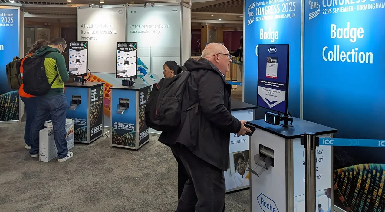 People scanning their e-badges and collecting their badges from PrintPods in foyer